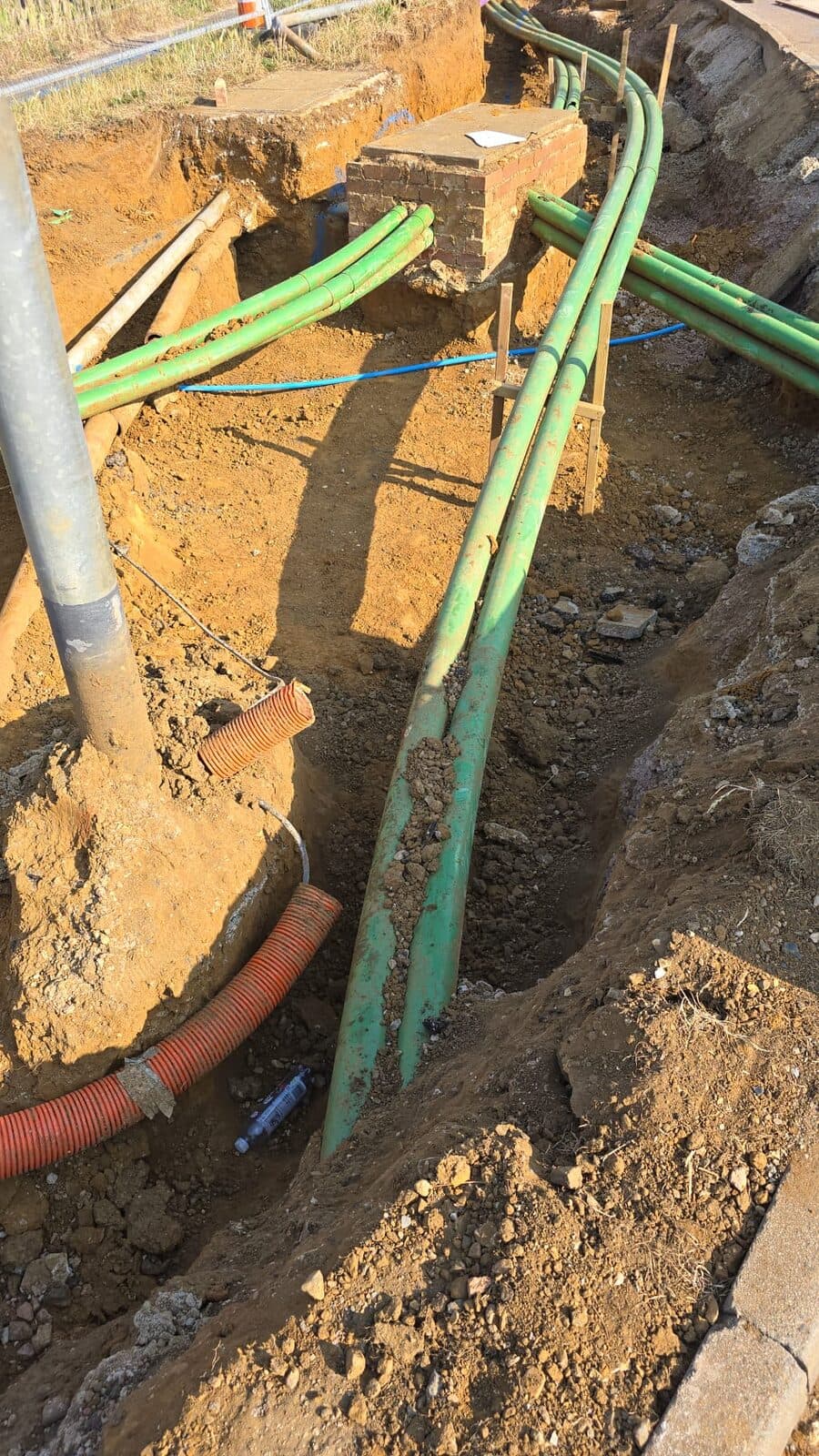 Close-up of green ducting cables exposed in narrow trench with wooden support stakes at excavation site